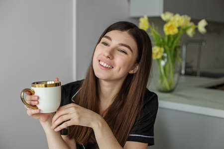 Adorable young brunette smile. Beautiful black pajamas. Beautiful vase with yellow flowers. Cozy...