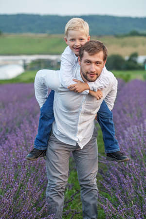 Young happy father having fun together and walking with little son in lavender field in summer. Dad and child spend time on weekends in countryside.の写真素材