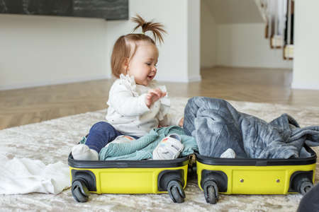 Happy little girl toddler tourist packs clothes in suitcase for travel, vacation. Baby clothes and...