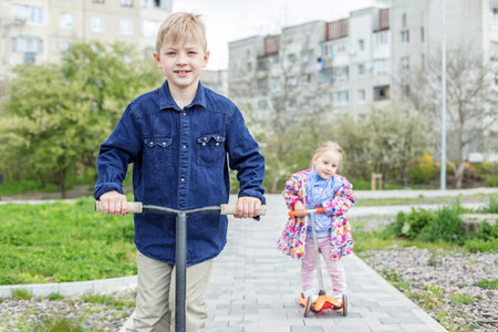 Little blond boy and girl ride kick scooters. Children play in playground on sunny spring day. Healthy outdoor activities. happy family.の写真素材
