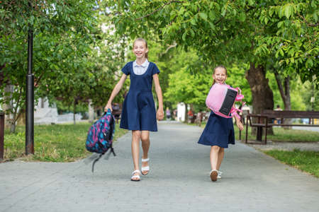 Two schoolgirls go from school and throw backpacks. Children are having fun. Concept back to school, learning, friendship and childhood.の写真素材