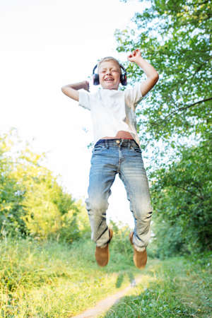 Teenage boy listens to song, jumps and dances. Blond boy uses headphones. Concept of music, radio...