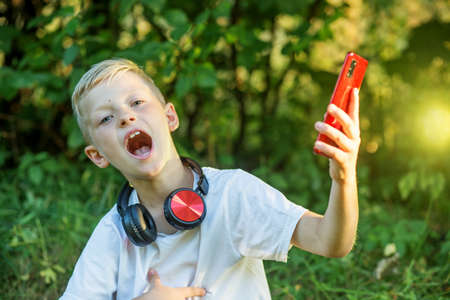Boy communicates via video chat using smart phone and Internet. Child laughs emotionally. Technology and childhood concept.の写真素材