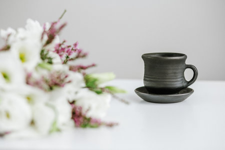 Black ceramic cup with coffee on table and bouquet of flowers. Copy space.の写真素材