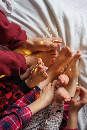 Family with children resting in bed. Christmas lights. Flat lay. Beautiful background. Night.の写真素材