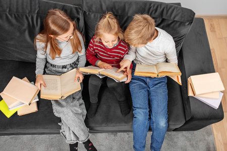 Three children read books sitting on sofa in room. World book day concept, lifestyle, study, education. Many books.の写真素材