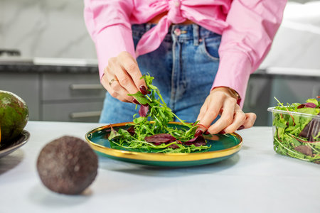 Woman is preparing salad from vegetables and spring mix in kitchen. Concept of healthy food, diet...