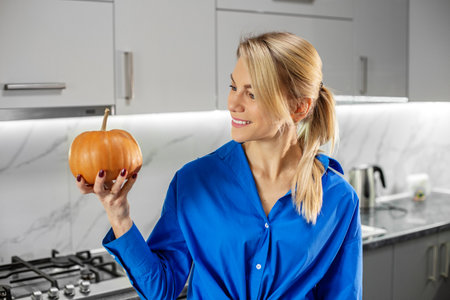 Thanksgiving Day. Portrait of blonde woman with pumpkin in kitchen. Copy space.の写真素材