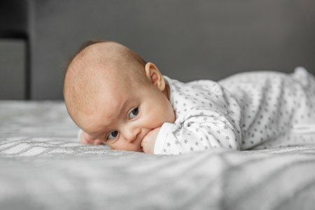 Child care concept. Portrait of cute little baby in bodysuit lying on blanket at home. Selective...
