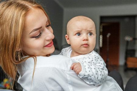 Mother takes care of her newborn baby at home. Mom holds her little two-month-old daughter in her...