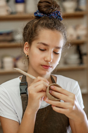 Beautiful teenage girl playing with modeling clay in pottery workshop. Craft and clay art....