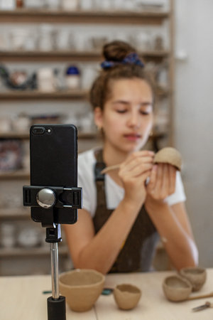 Craft and clay art. Children's creative. Arts education. Teenage girl playing with modeling clay in pottery workshop, learning online using smartphone.の写真素材