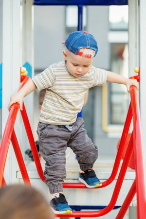 Cute two year old boy plays on playground slide on summertime. Kid play on kindergarten yard. Active kid on colorful slide and swing.の写真素材
