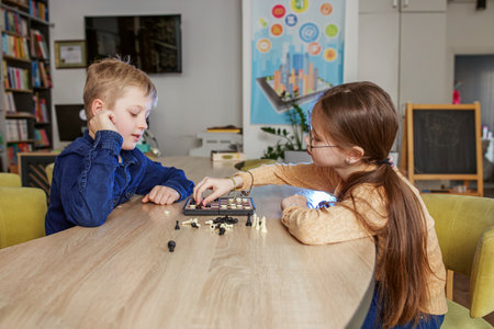 Caucasian boy and girl playing checkers, sitting together at table in school. Little friendly classmates.の写真素材