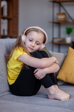 Unhappy little girl in headphones sitting in sofa at home. Concept mental health.の写真素材