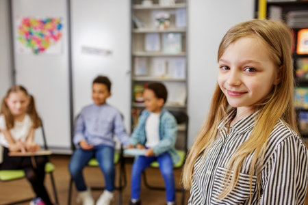 Schoolgirl standing in middle of classroom and answering question in front of classmates and teacher. Back to schoolの写真素材