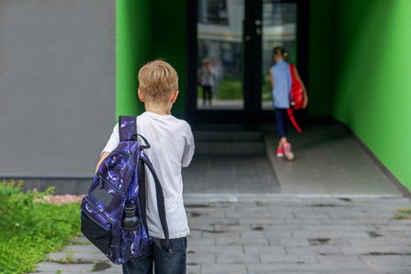 Small students, boy and girl, approach to door of school. Children with school backpacks. Back to school.の写真素材