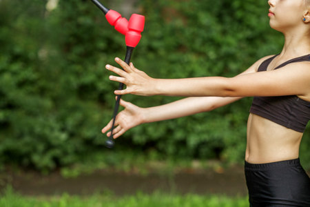Rhythmic gymnastics. Children's hands with gymnastic mace on background of park. Copy space. Little sporty girl exercising with gymnastic mace outdoorの写真素材