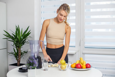 Healthy food concept. Blond smiling woman making smoothie at home kitchen.の写真素材