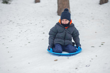 Child boy ride in snow plate. Outdoor play. Cold temperature. Winter timeの写真素材
