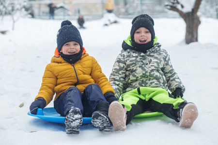Children ride on snow plate and having fun. Outdoor play. Cold temperature. Winter time.の写真素材