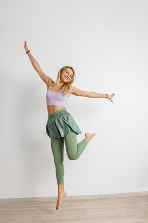 Happy athletic woman dancing in modern fitness attire, with bare feet on a wooden floor, white background.の写真素材