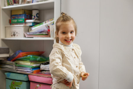 Cheerful kid with ponytail smiles brightly in colorful playroom setting.