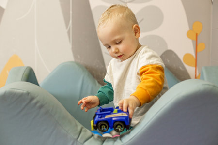 Little child is focused on playing with a colorful toy truck in playfully decorated room.