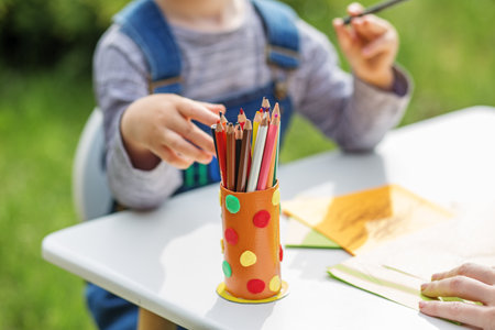 Close up of kid choosing colored pencils from holder while engaging in drawing activity outdoors.の写真素材