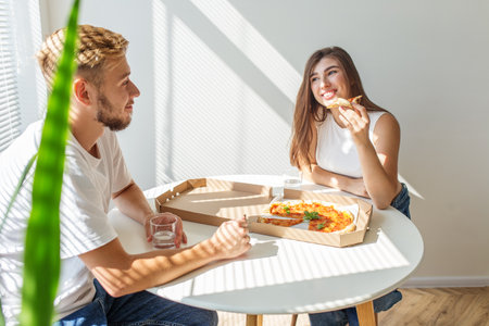 Pregnant woman and her partner enjoy pizza together in sunlit dining area, sharing smiles and relaxed, happy moment.の写真素材