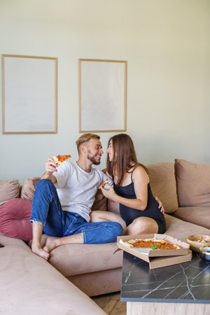 Happy family sits on couch, sharing and enjoying pizza together, showcasing cozy and intimate moment at home.の写真素材