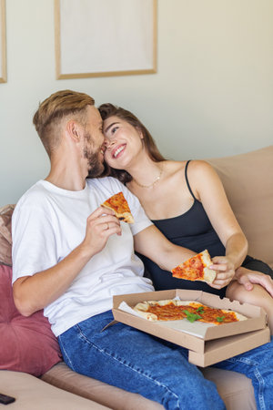 Joyful couple enjoys sharing pizza while sitting close on couch, capturing moment of love and happiness at home.の写真素材