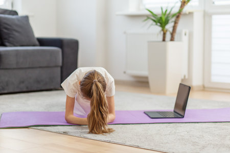 Tween girl following an online yoga class while practicing yoga pose on mat at home, focusing on strength, flexibility, and mindfulness.の写真素材