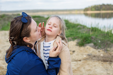 Mother gently comforts upset child near calm riverbank, offering support and love in peaceful outdoor setting.の写真素材