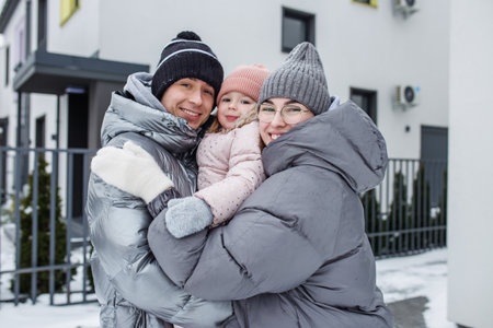 A happy family poses outdoors in winter attire, smiling and embracing each other. The scene features...