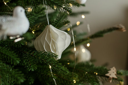 A beautifully decorated Christmas tree features delicate white ornaments and warm string lights, creating a cozy atmosphere in a living room during the holiday season.の写真素材