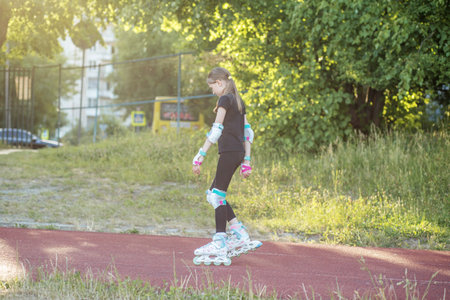 A young girl in protective gear is practicing roller skating on a red track in a park during the afternoon.の写真素材