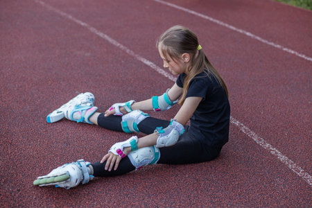 Child sits on the track after falling while roller skating. She is wearing protective gear and...