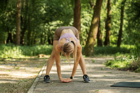 A fitness enthusiast performs a forward bend stretch in a serene park surrounded by vibrant trees. The sunny morning creates a refreshing atmosphere for outdoor exercise.の写真素材