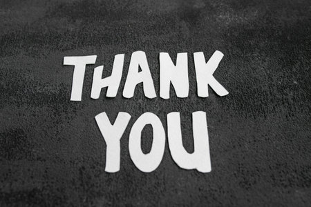 White cutout letters arranged to say thank you are placed on a dark, textured surface. This artwork emphasizes gratitude and appreciation through simple design elements.の写真素材