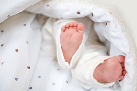 Small baby feet peek out from a cozy and soft blanket decorated with tiny hearts. The infant is nestled comfortably, showcasing delicate toes and smooth skin.の写真素材