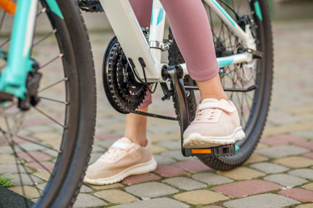 Detailed view of a young girl's feet on bike pedals, highlighting cycling motion and sporty footwear on a paved sidewalk.の写真素材