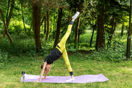 Young girl practices a challenging yoga pose with one leg raised high in a forest, focusing on strength, flexibility, and control.の写真素材