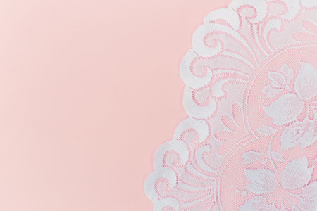 Delicate white lace with floral pattern displayed on a pale pink backdrop, ideal for romantic, vintage, or wedding design themes.の写真素材