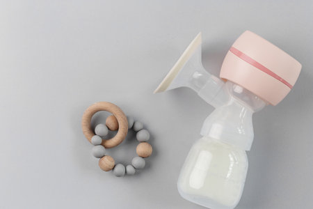 Top view of a modern electric breast pump filled with milk beside a wooden and silicone baby teether...