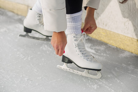 Close-up of a woman lacing white figure skates, preparing to skate on a frozen outdoor rink in...