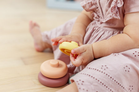 Close-up of babyâs hands holding soft pastel rings while seated on the floor, promoting fine motor skills and early learning.の写真素材