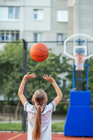 Back view of a child shooting a basketball toward the hoop on an outdoor urban court. Captures motion, confidence, and youth sport.の写真素材