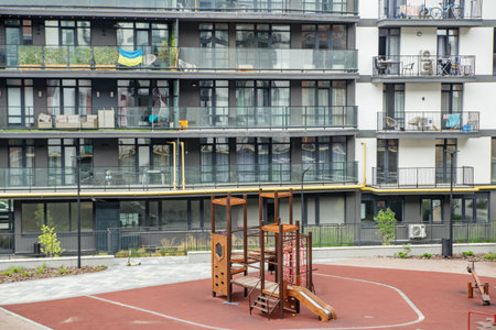 Urban playground area in front of contemporary apartment complex, featuring climbing structures, slide, and safety flooring for children.の写真素材