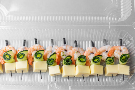 Appetizer skewers with shrimp, cucumber spirals, and cheese cubes neatly arranged in a clear plastic tray for catering or delivery.の写真素材